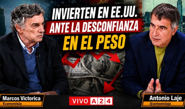 Two men in a TV debate sit facing each other against a backdrop filled with money, with bold Spanish headlines about investing in the U.S. and the strength of the dollar, and a "VIVO A24" banner.