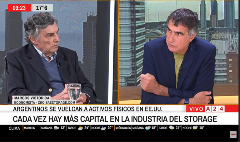 Split-screen TV interview: left, older man in blazer; right, man in blue blazer with lime shirt; newsroom backdrop; bottom ticker about the storage industry.